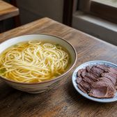 A bowl of fine yellow wheat noodles beside a plate of sliced braised donkey meat