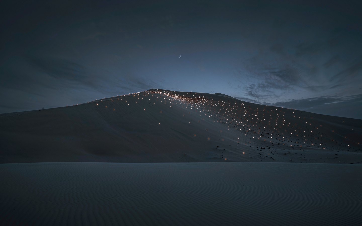 Thousands of phone lights dotting a huge sand dune at night