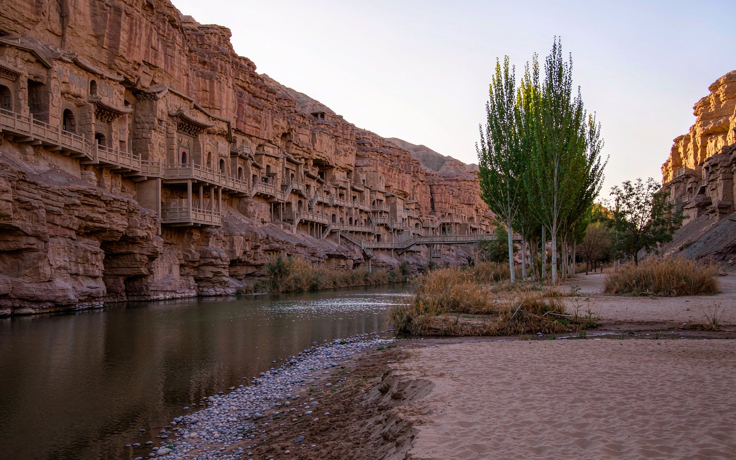 Cliff-face grottoes above a green river valley in the desert