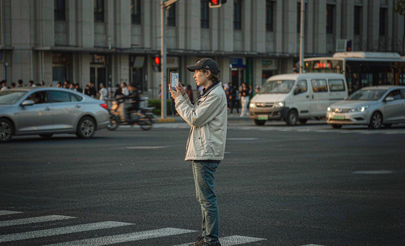 A foreign traveler at a Chinese city crosswalk holding up a smartphone with a map route on the screen