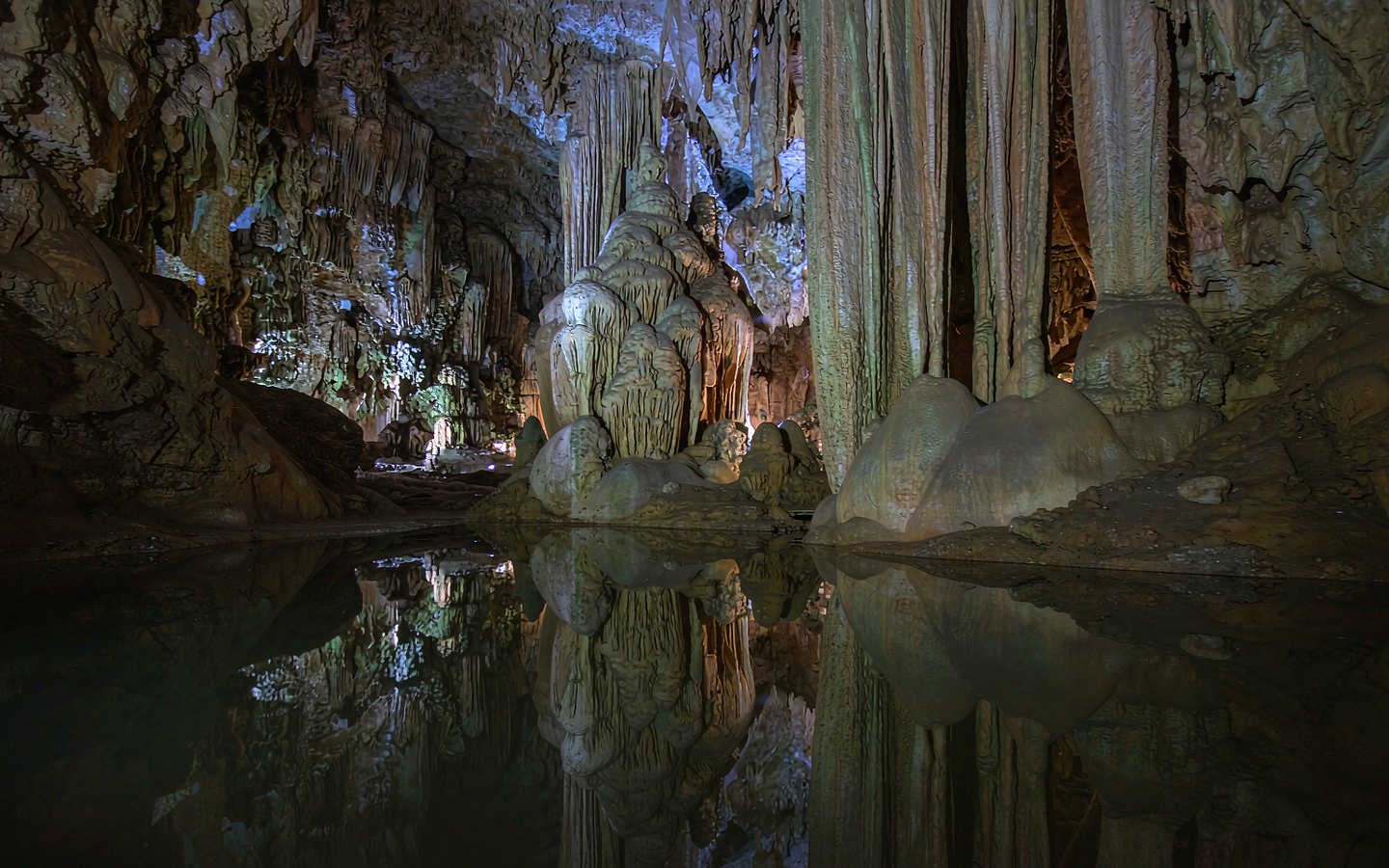 Colour-lit stalactites reflected in a still underground pool