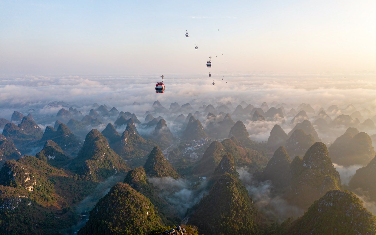 Cable cars crossing above a sea of karst peaks at dawn
