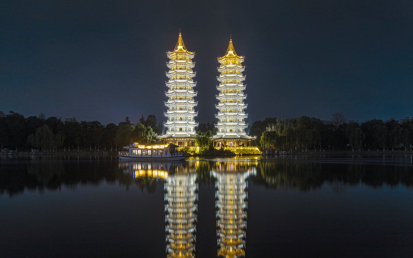 Gold and silver pagodas lit up on a dark lake at night