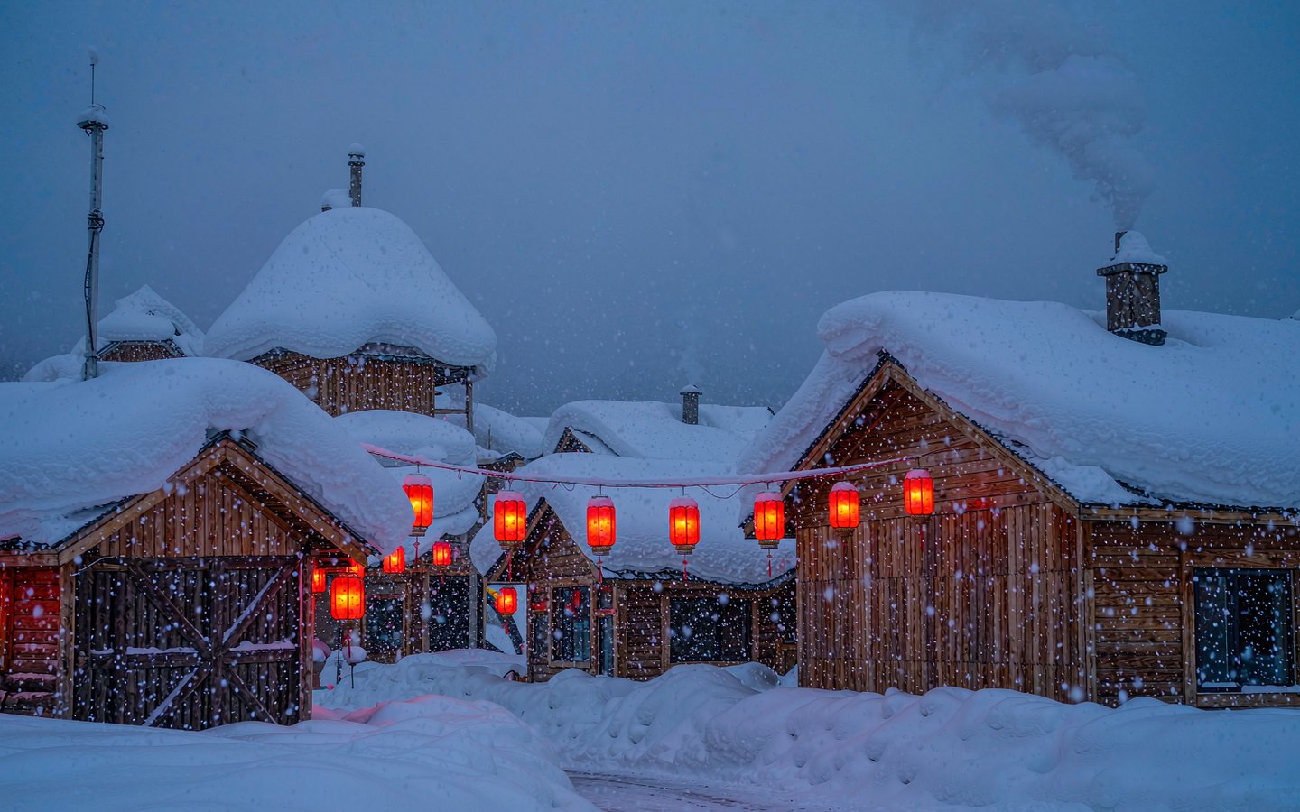 Snow-buried wooden houses glowing with red lanterns at night