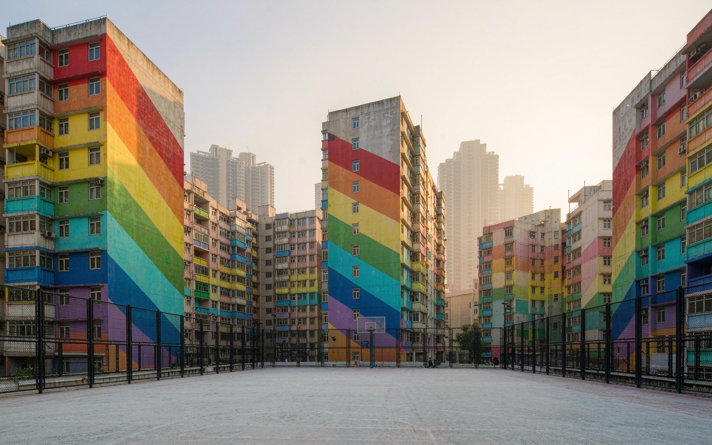 Basketball court on a rooftop framed by rainbow-coloured housing blocks