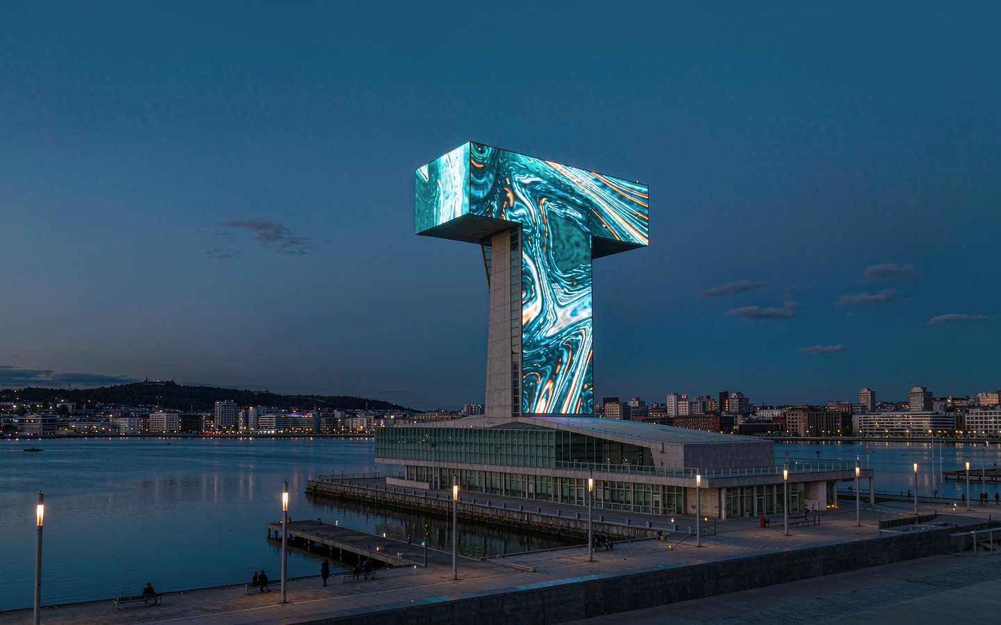 Inverted-T museum tower glowing beside the harbour at dusk