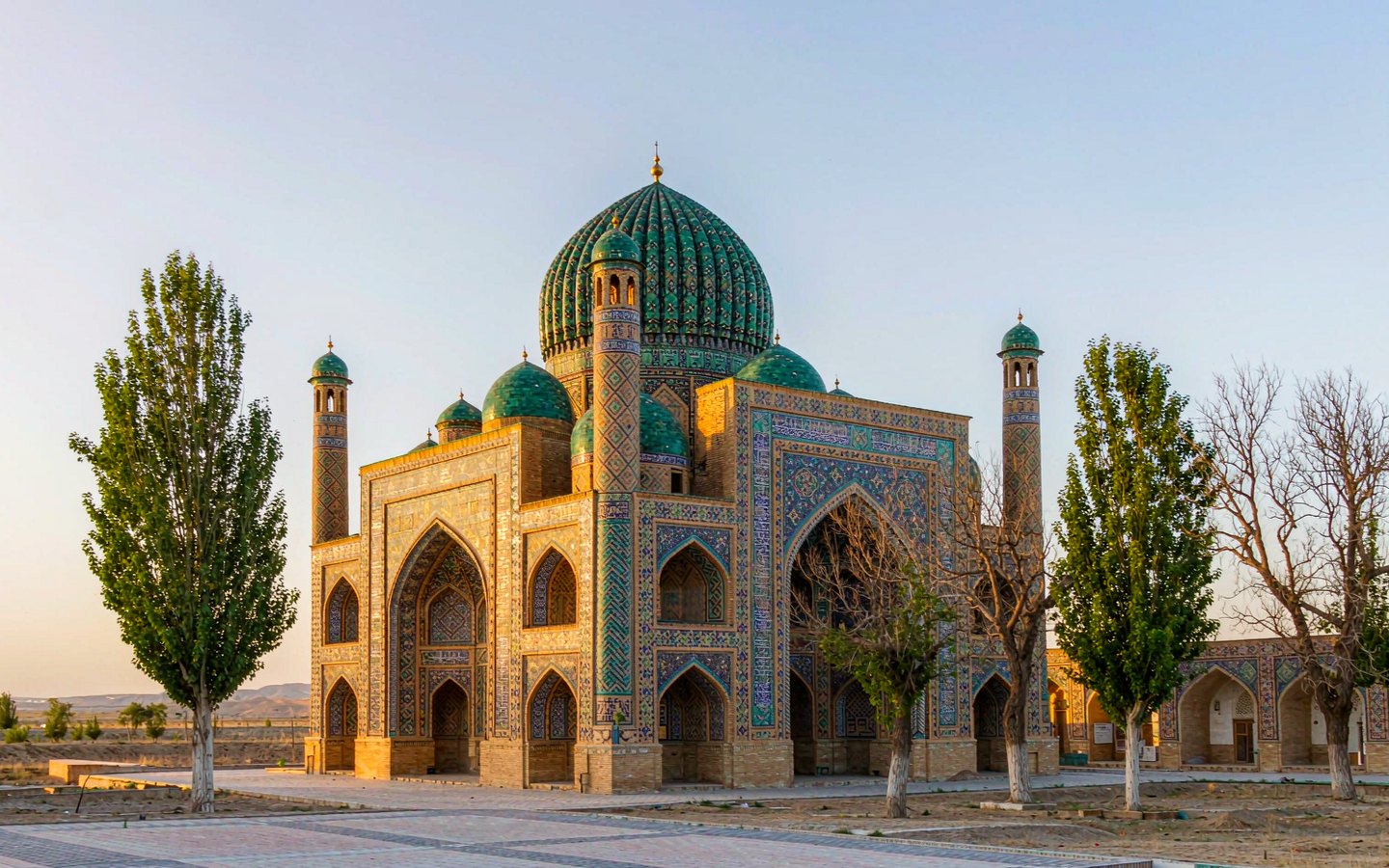 Green-tiled domed mausoleum with minarets under a desert sky