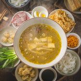 A bowl of scalding golden chicken broth with raw meat, quail eggs and rice noodles in small dishes on a dark wooden table