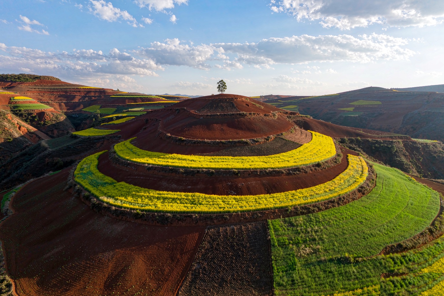 Rolling hills striped with iron-red soil and bands of green and gold farmland in the Dongchuan Red Land, Yunnan
