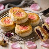 Round flaky golden pastries with dark red rose petal filling cooling on a griddle tray at a Kunming bakery