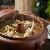 A brown Jianshui clay steam-pot with a central spout, lid lifted to show clear golden broth with chicken pieces and goji berries