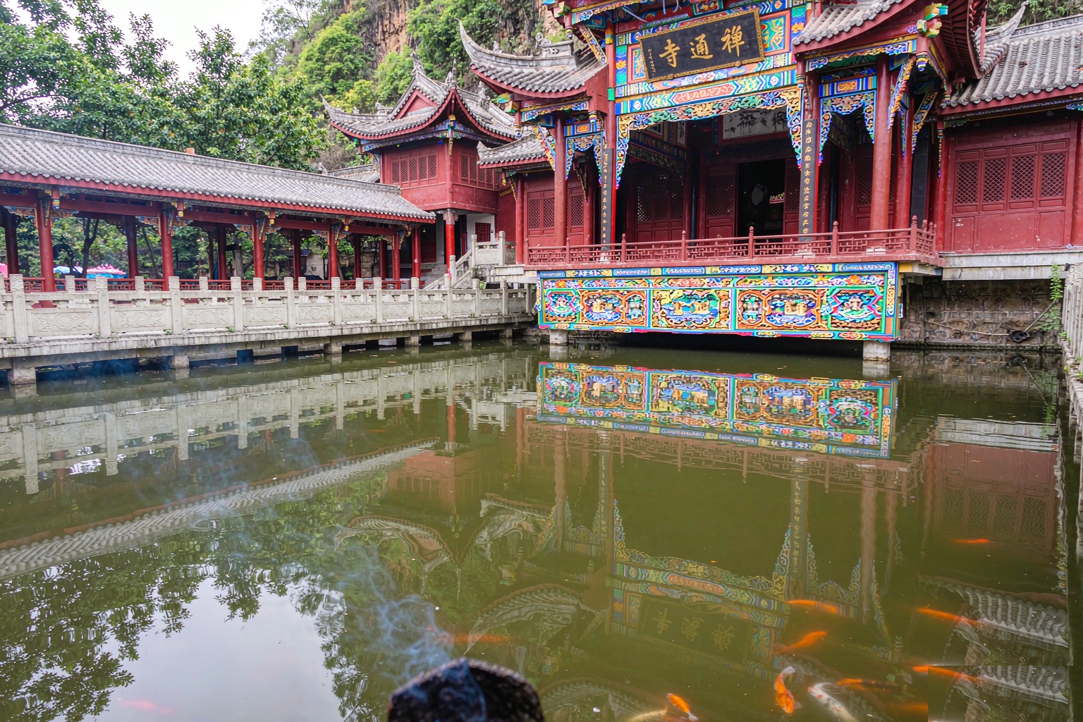 The Buddhist temple hall with upturned tiled roofs and red pillars reflected in the pond at Yuantong Temple, Kunming