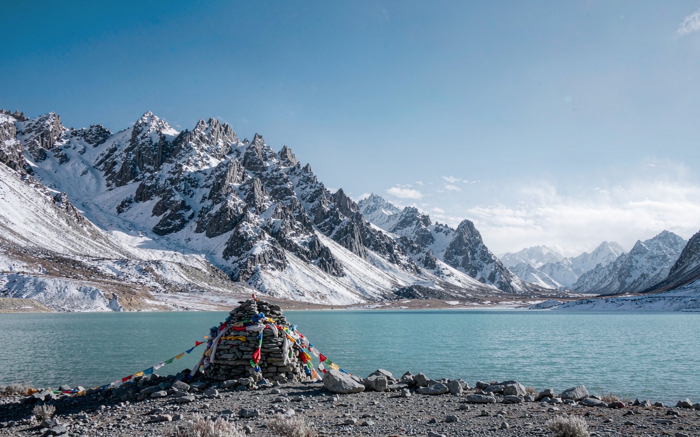 Turquoise sacred lake under snow peaks with prayer flags on the shore