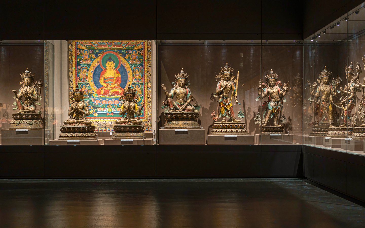 Gilded Buddhist statues and thangkas in a hushed museum hall
