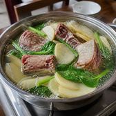 A pot of clear broth with cured pork ribs, potato and greens on a table burner