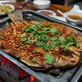 A whole fish grilled on a metal tray under chilli, garlic and coriander
