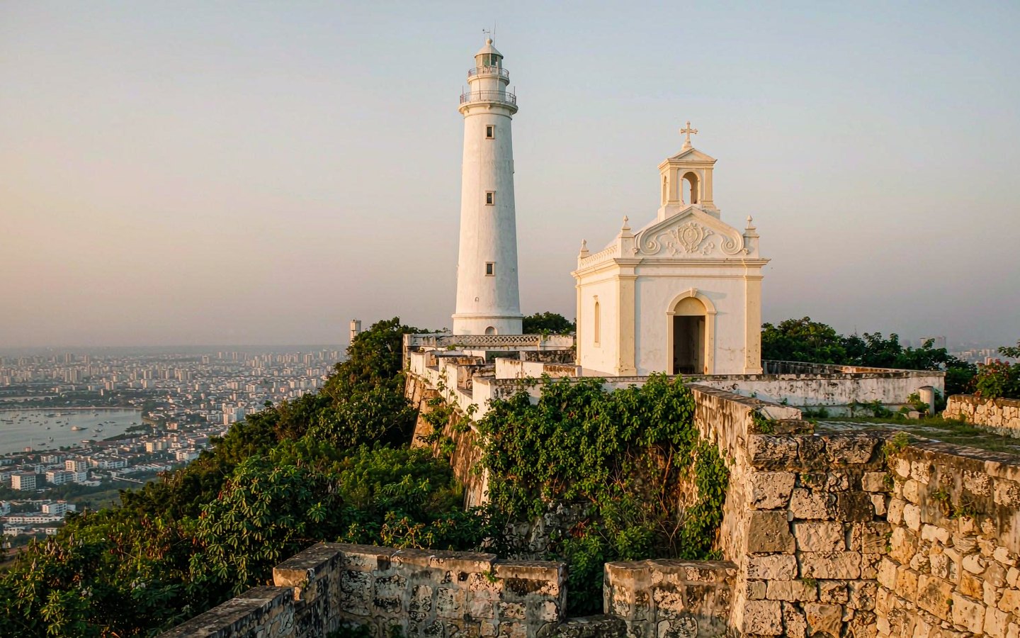 White lighthouse and chapel on a green hill above the city