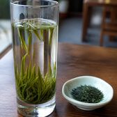 Needle-shaped green tea leaves standing in a tall glass of hot water