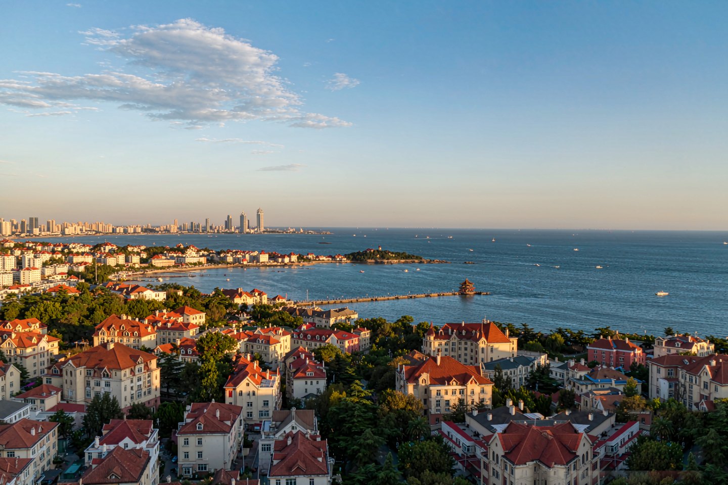 Qingdao's red-roofed old town and Zhanqiao Pier curving into the bay, seen from the hills above