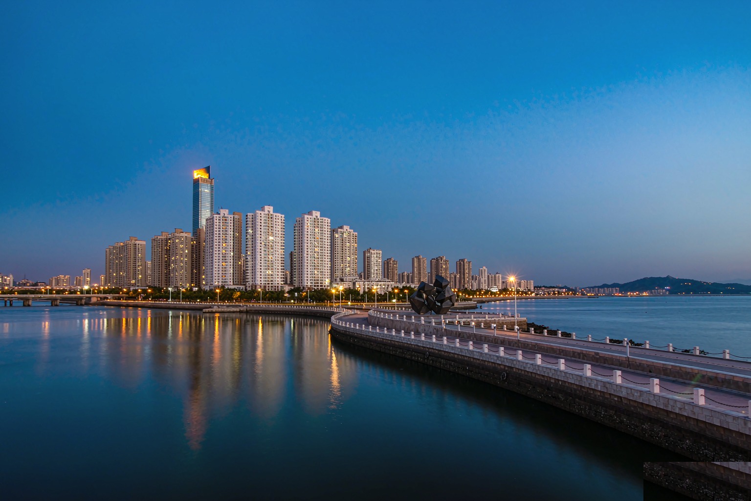 Qingdao's Fushan Bay coastal skyline at dusk with the Olympic rings sculpture lit on the waterfront