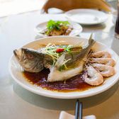 A whole steamed fish with ginger and spring onion and a plate of white boiled prawns on a Cantonese restaurant table