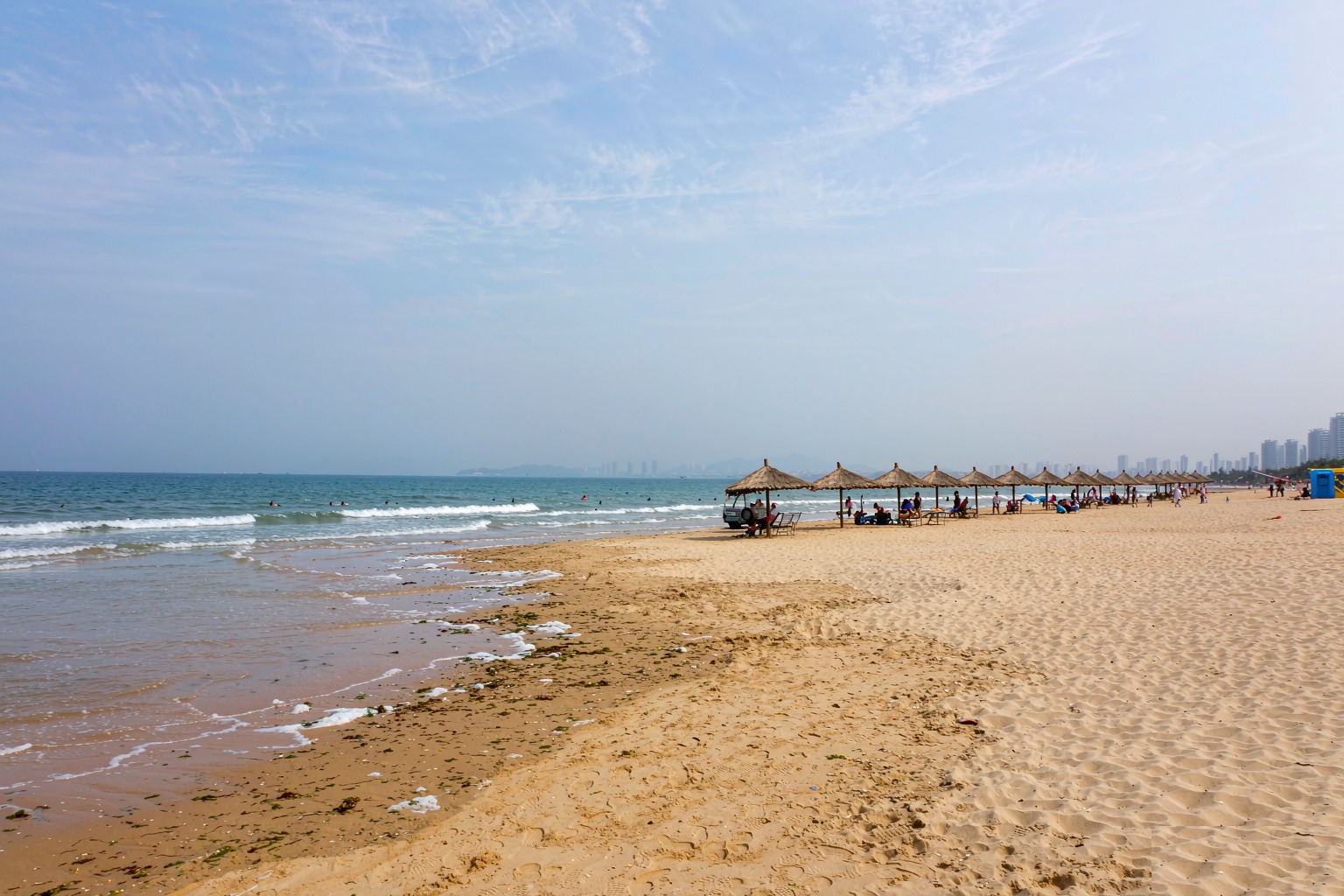 Golden sand and thatched umbrellas at Dameisha Beach on a summer day