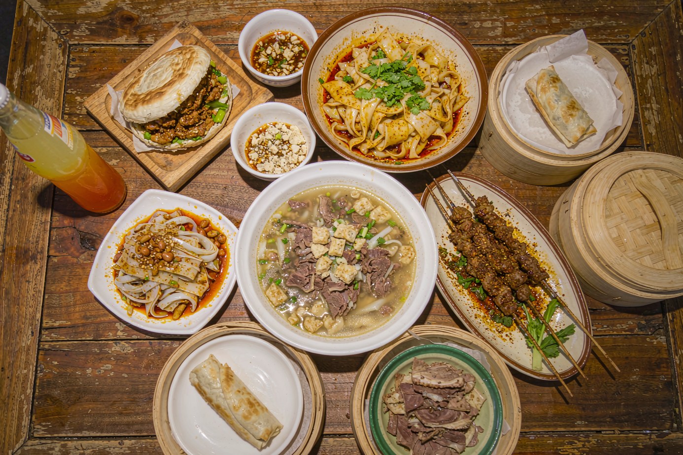 Overhead spread of Xian street food: roujiamo, paomo, liangpi, noodles and an Ice Peak soda