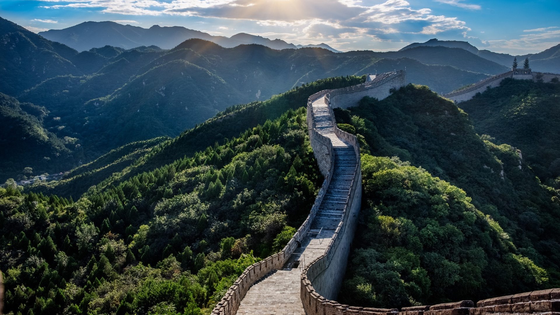 The Great Wall climbing a forested ridge in afternoon light, its walkway empty of visitors
