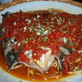 A split fish head buried under chopped red chilli, garlic and spring onion, over rice noodles