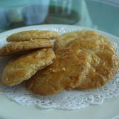 Half a dozen pale golden almond cookies with crackled tops, stacked on a white paper doily on a plate.