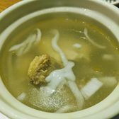 A ceramic pot of clear coconut broth with curls of white coconut flesh and a piece of bone-in chicken.
