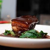 Close-up of braised pork belly with sauce and greens on a ceramic plate.