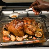 Delicious baked chicken with roasted vegetables being basted in a kitchen setting.