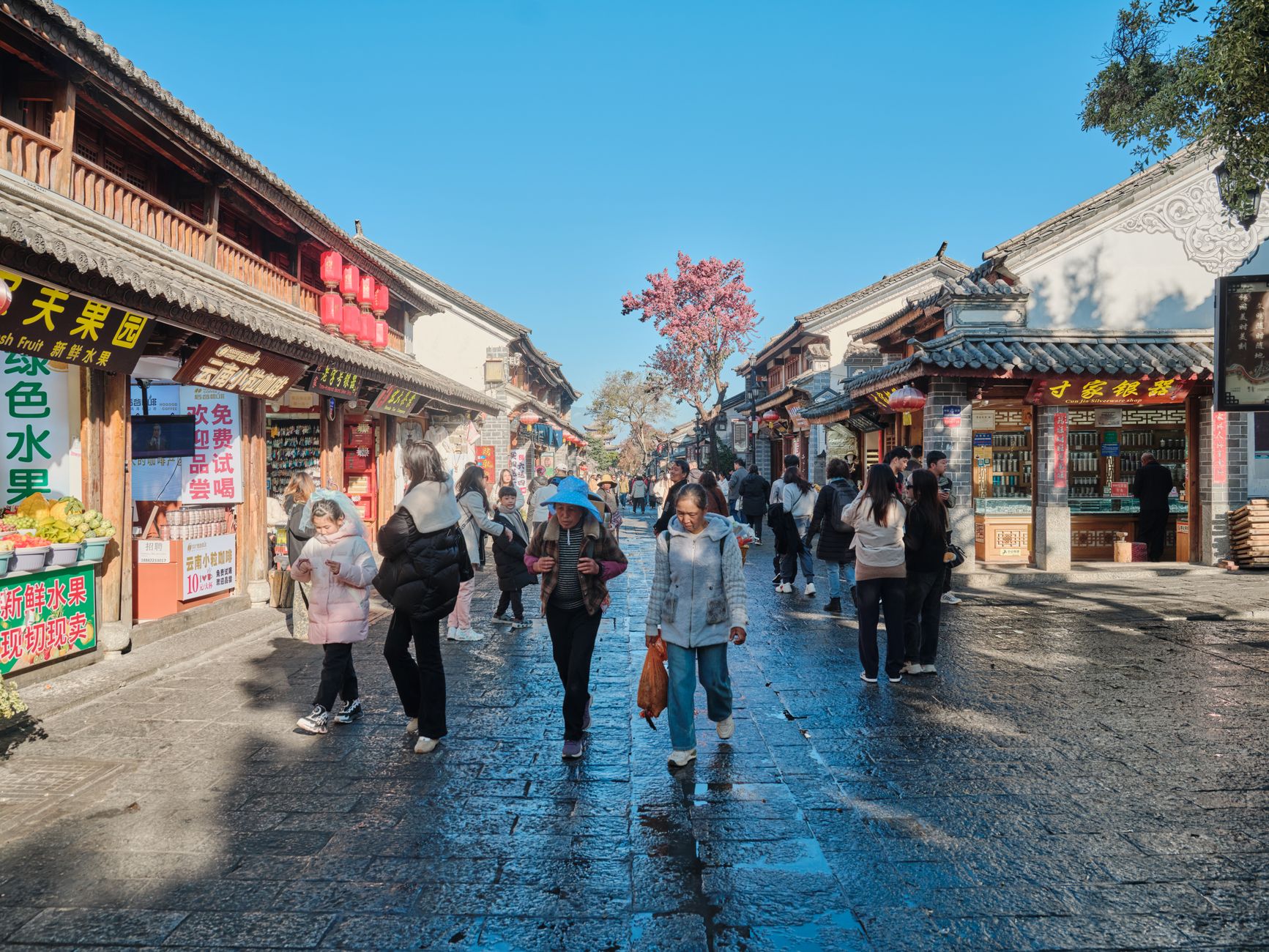 Vibrant street market in a traditional Chinese town with people shopping on a sunny day.
