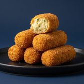 A stack of breadcrumbed croquettes on a dark plate, the top one broken open to show a pale, herb-flecked filling.