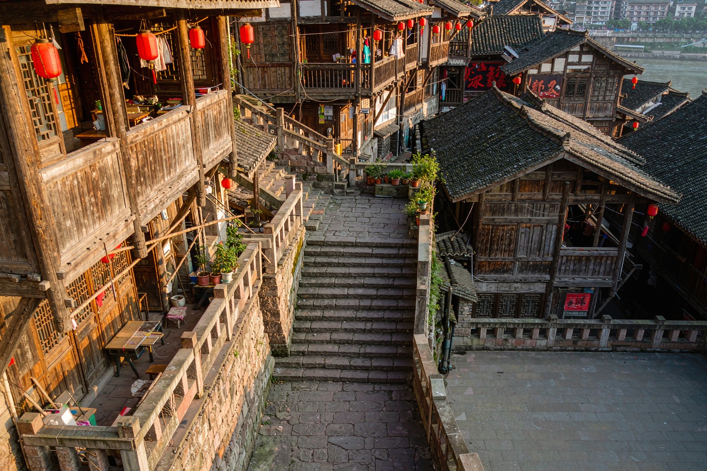 Steep stone steps descending between weathered wooden stilt houses with red lanterns in an old Chongqing neighbourhood