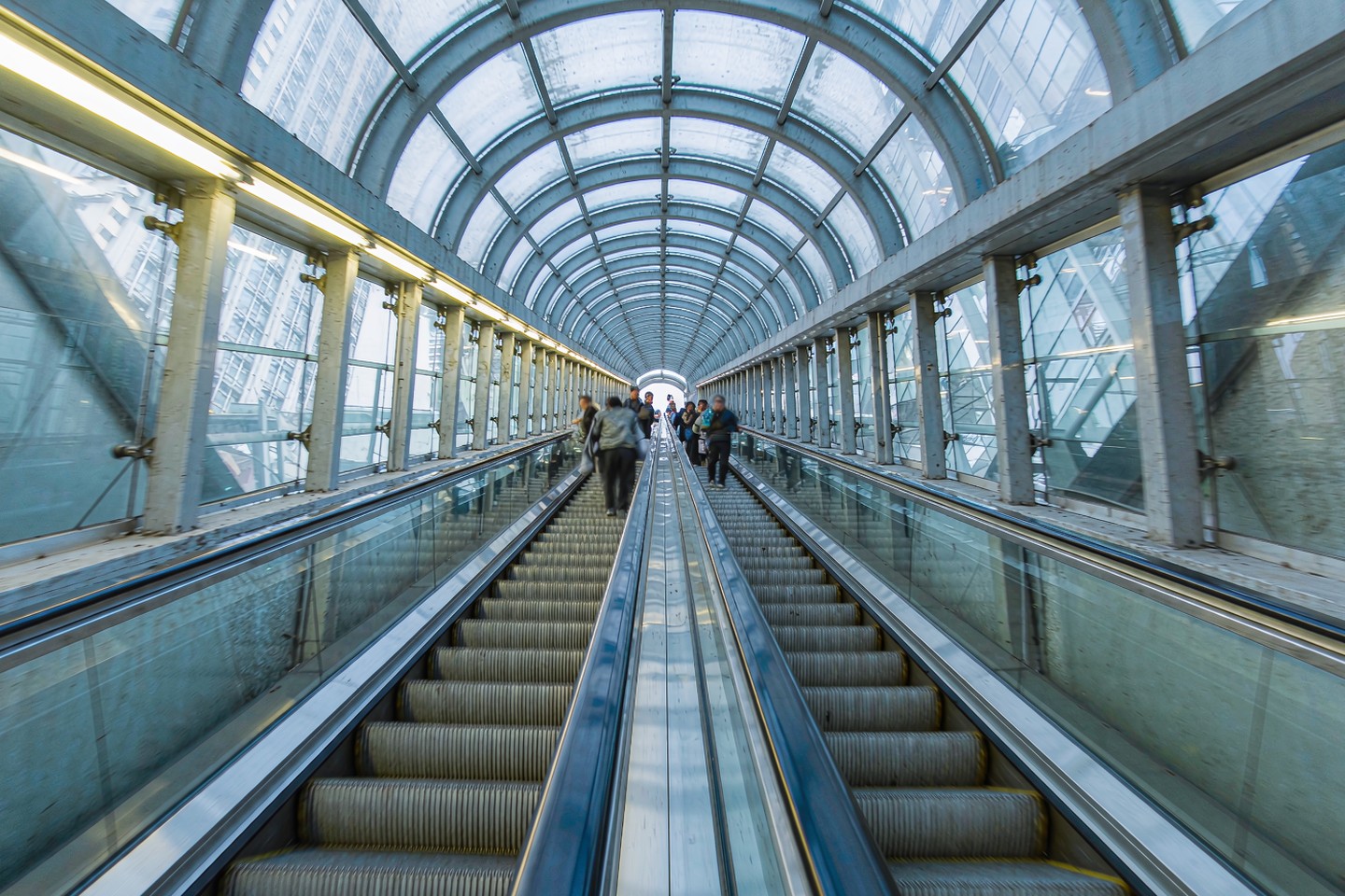 A long steep double escalator descending through a glass-roofed concrete tunnel in a Chinese metro station