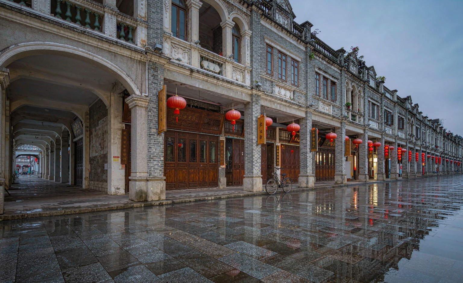 Arcaded qilou shopfronts, red lanterns and a wet stone street in old Guangzhou