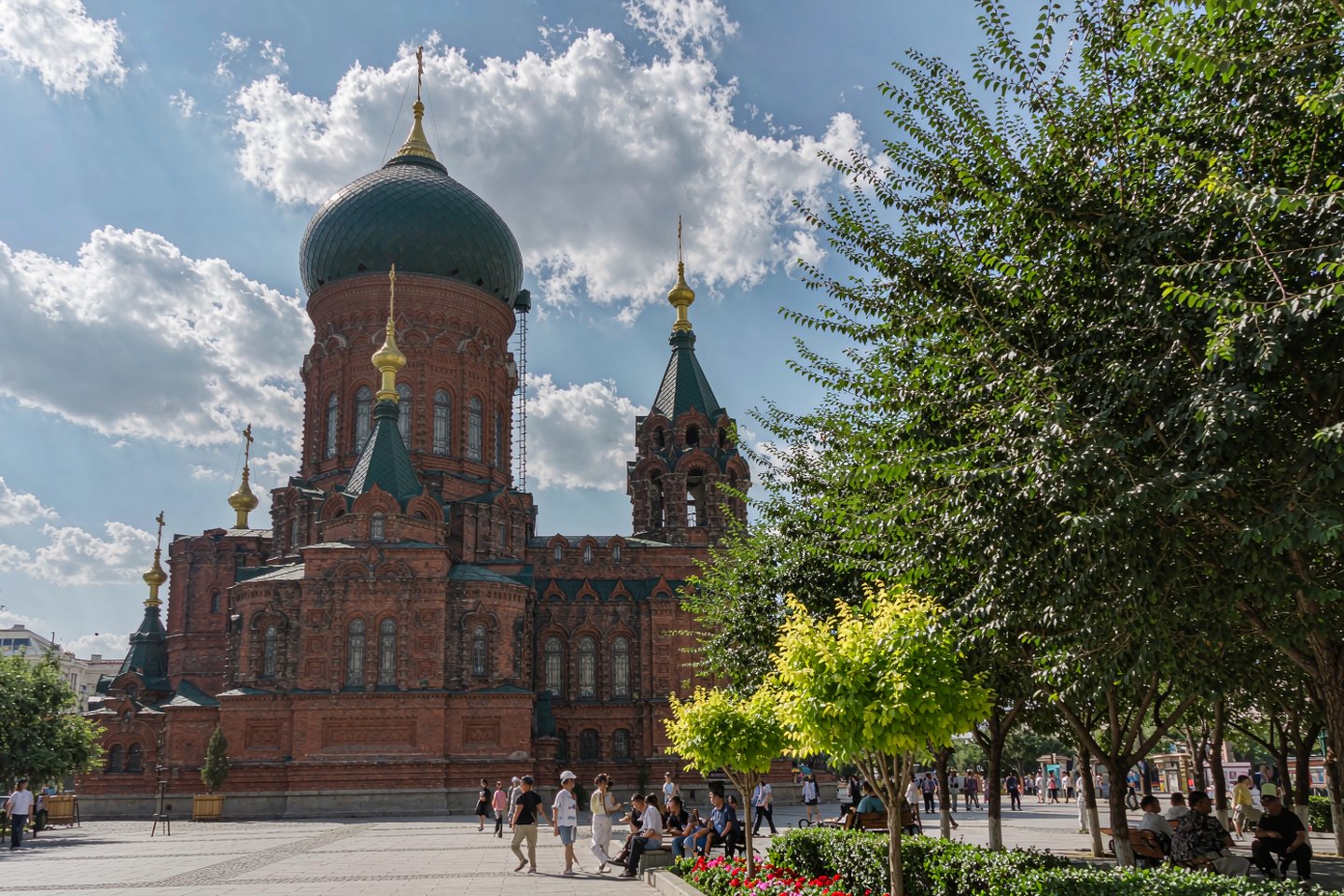 Saint Sophia Cathedral in Harbin under a summer sky, red brick and green domes among full-leafed trees