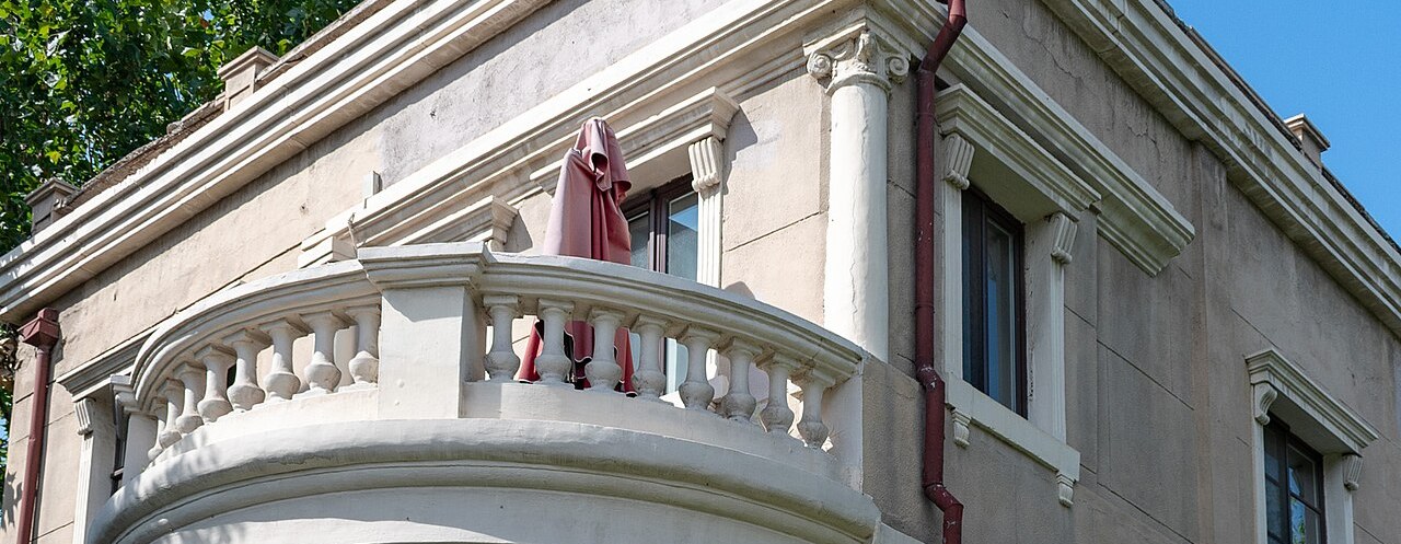 A white Italianate villa with a curved balcony among clipped hedges in the Italian Style Town